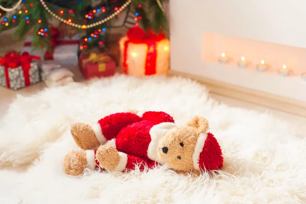 Santa tedyy bear toy on sheepskin near illuminated christmas tre — Stock Photo, Image