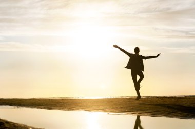 Güneş batımında sahilde genç dans eden kız siluet.