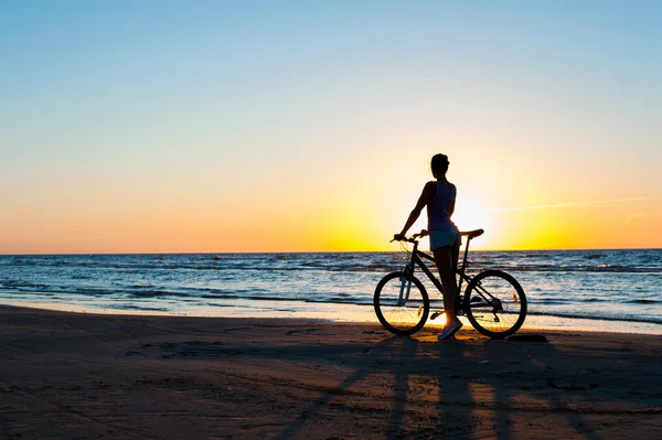 Momento en el tiempo. Mujer ciclista silueta en la puesta de sol multicolor — Foto de Stock