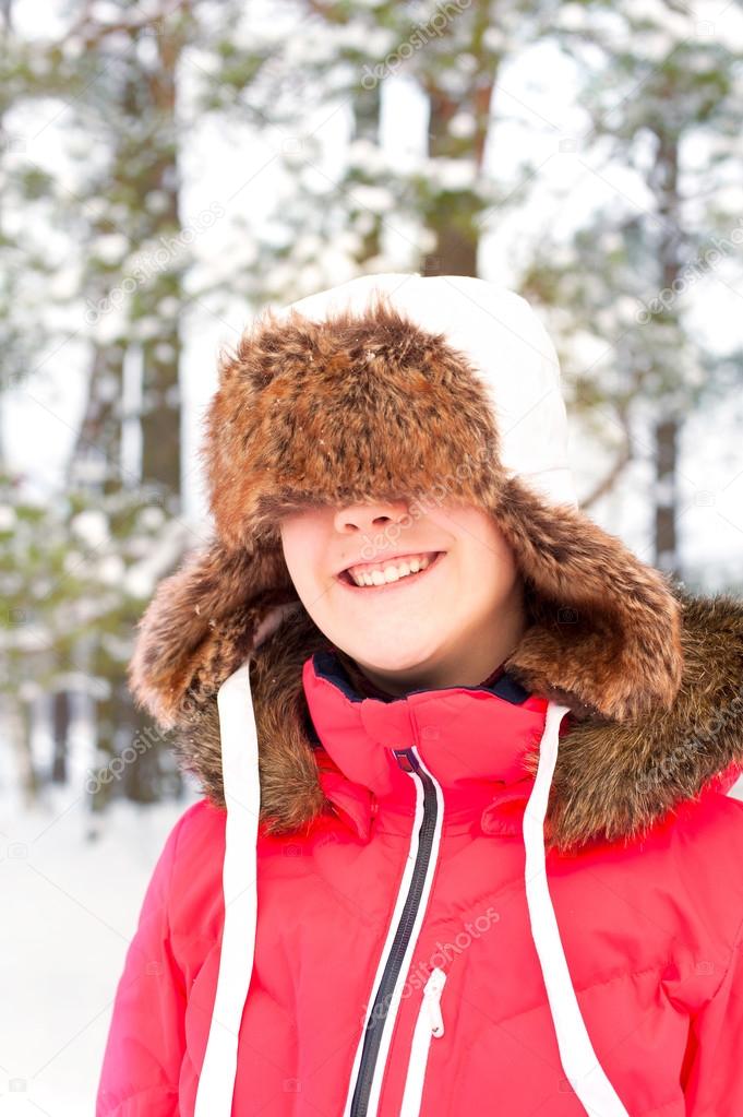 Funny cheerful laughing girl in warm earflap in winter forest