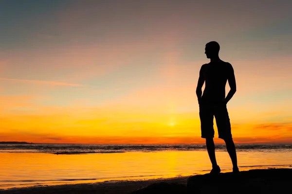 Young sporty man silhouette standing on the beach at sunset — Stock Photo, Image