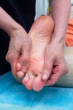 Masör ayak masajı yapıyor. Kendi elleriyle, ayak ve bacağa masaj yapıyor..