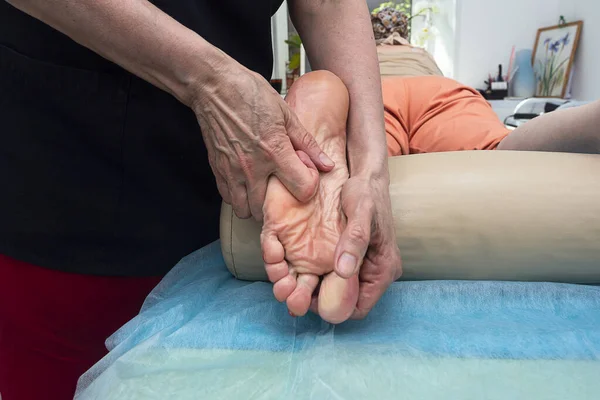 Masör ayak masajı yapıyor. Kendi elleriyle, ayak ve bacağa masaj yapıyor..