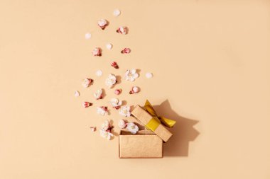 Sarı arka planda kurdeleli hediye kutusu ve dağınık bahar çiçekleri. Neşeli arkaplan.