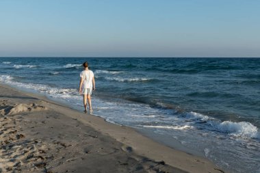 Genç kız gün batımında sonsuz kumlu sahilde yürüyor..