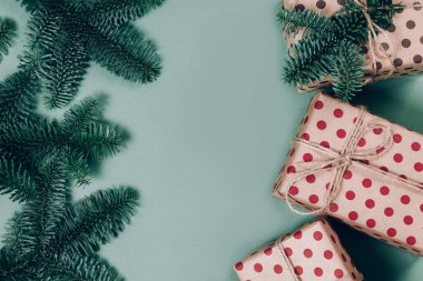 Açık yeşil arka planda çeşitli renkli hediye kutuları ve Noel kozalaklı dalları..