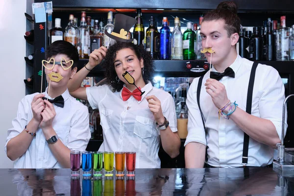 Three waiters with festive props and LGBT shots in a bar. Funny and friendly waiters wearing bow tie in a pub.