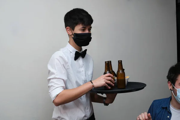 女服务员戴着防护面罩 给客人们端来饮料 酒吧里的新常态 — 图库照片