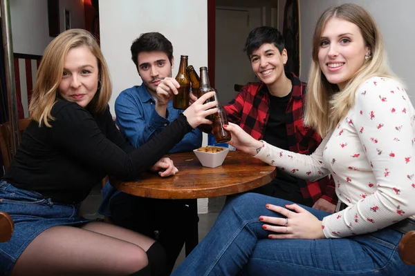 四个微笑的朋友在酒吧里举着啤酒瓶敬酒 看着镜头 友谊概念 — 图库照片