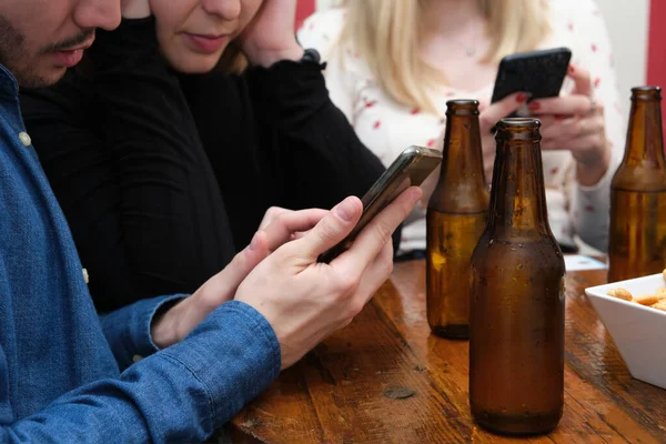 三个不认识的朋友在智能手机上看到了什么 在酒吧里喝酒 友谊概念 — 图库照片