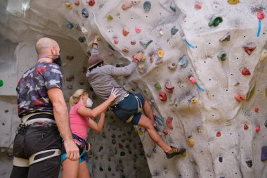 Koruyucu yüz maskeleri takan üç genç arkadaş yapay kaya duvarlarına tırmanıp birbirlerine yardım ediyorlar. Yeni normalde ekstrem sporlar.
