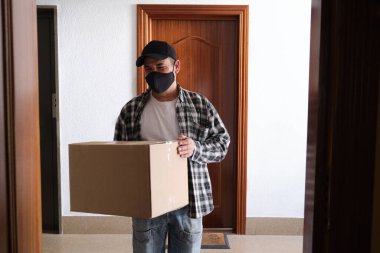 Paket taşıyan bir teslimatçı kapıda bekliyor. Karantina, hastalık salgını, koronavirüs covid-19 salgını altında teslimat hizmeti.