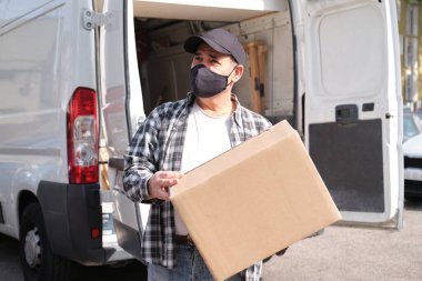 Karavanının önünde elinde bir paketle bekleyen son sınıf bir teslimatçı. Karantina, hastalık salgını, koronavirüs covid-19 salgını altında teslimat hizmeti.