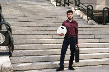 Elinde panda maskesi ve merdivenlerde duran bavulu olan genç bir iş adamı. Tuhaf iş adamı..