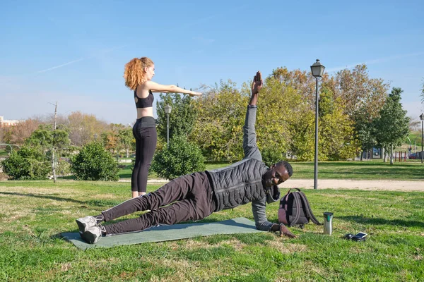 African black man and redhead caucasian woman exercising in a park with a mat. Fitness and sport outdoor.