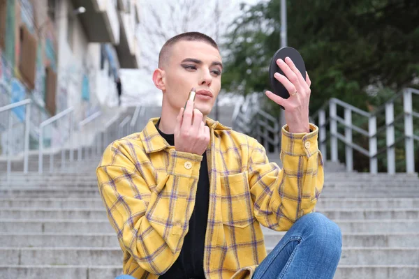 Yakışıklı bir gencin portresi, aynanın önüne ruj sürüyor, siyah bir göz farı takıyor, elinde makyaj fırçası tutuyor. Çift cinsiyetli olmayan erkek..