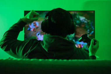 Kulaklık takan tanınmamış bir oyuncu, televizyon oyunlarında kazanılan zaferi kutluyor. Yeşil ışık biçimi.