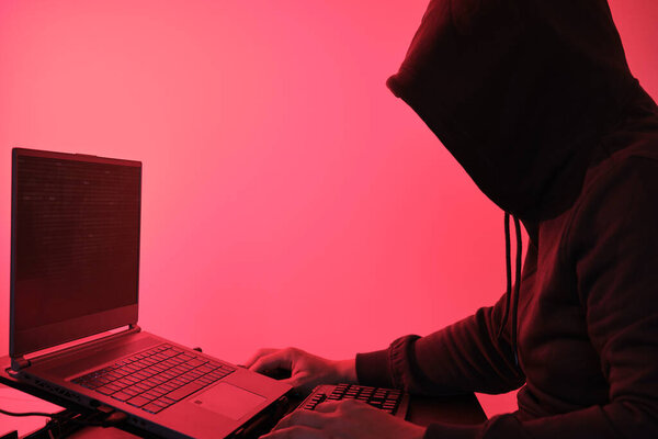 Хакер в капюшоне перед компьютером для организации массивной атаки на нарушения данных по всему миру. Киберпреступная концепция.