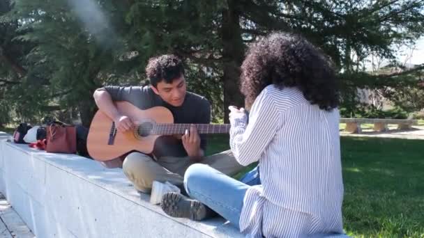 年轻的拉丁裔男子弹吉他 他的朋友在大学校园里用智能手机记录他 大学生活 千年一代 — 图库视频影像