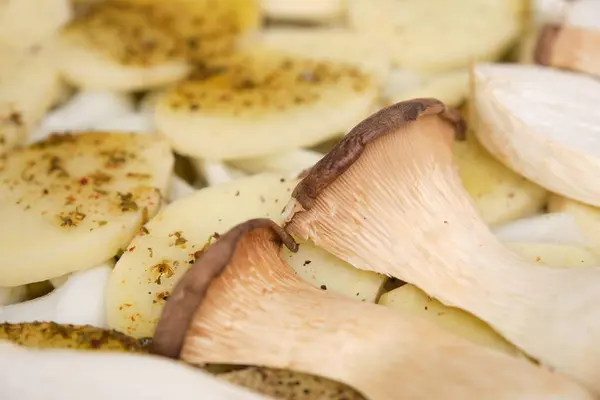 Closeup of sliced king trumpet mushrooms (pleurotus eryngii) over seasoned potatoes and onions. Cooking process. Mediterranean diet.