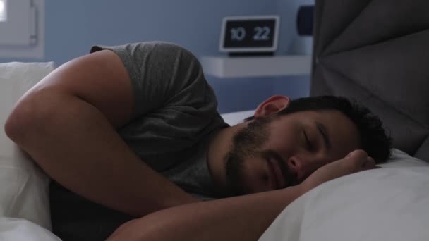 若いラテン系の男が朝遅く彼のベッドで寝ている 背景にデジタル時計 4Kビデオ — ストック動画