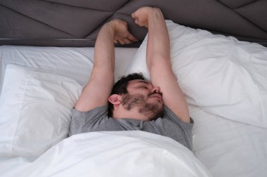 Genç latin adam uyuduktan sonra yatakta geriniyor. Uyku pozisyonu kavramı.