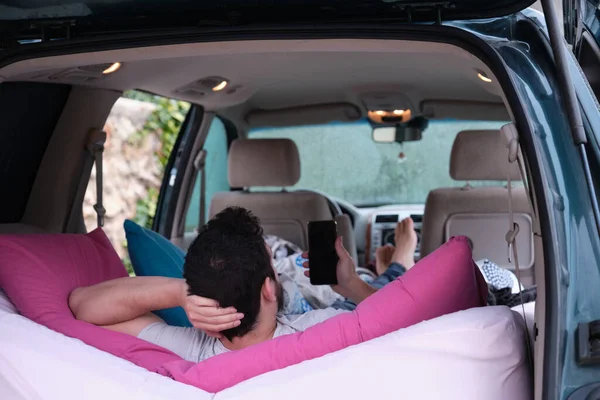 Adam rahatlıyor ve akıllı telefonunu arabasının içindeki bir yatakta kullanıyor. Özgürlük yolculuğu kavramı.