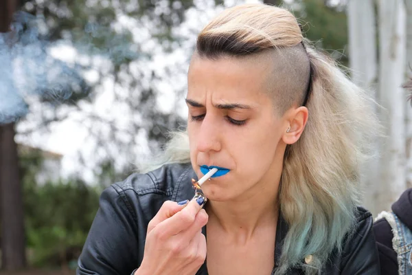 Young punk woman lighting up a cigarette in a park. Rock and roll lifestyle.