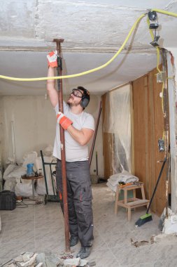 İnşaat işçisi ilk sütunu yerleştiriyor, bir çöküşü önlemek için destek ya da destek veriyor. Güvenlik eldiveni, gözlük ve kulaklık takan bir inşaatçı..