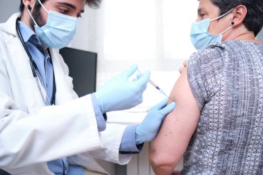 Klinikteki olgun kadın hastaya aşı yapan doktor. Covid-19 ya da koronavirüs aşısından önce elinde şırınga tutan hemşire..