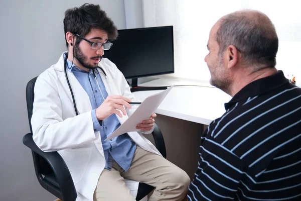 Young doctor health care professional talking with a senior man patient holding a paper and a pen. Medical prescription.