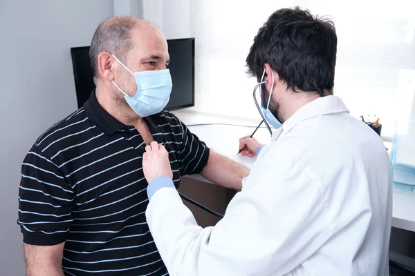 Joven Médico Escuchando Hombre Maduro Paciente Corazón Con Estetoscopio Anotando —  Fotos de Stock
