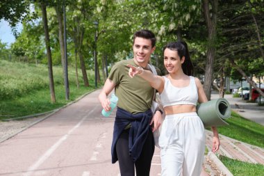 Genç spor çifti bir şeyi ya da bir yeri gösterip gülümsüyor. Fitness dışarıda.