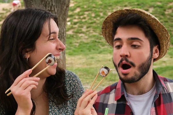 夏の晴れた日にピクニックをする公園で寿司を食べて笑っている若い幸せなカップル — ストック写真