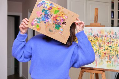 Genç mutlu kadın ressam paletine bakıyor. Sanatçı tuvale resim yapmaya hazır.
