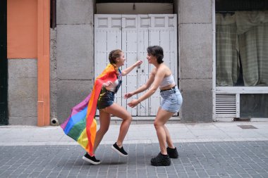 Igbt bayrağı pelerin gibi bağlanmış bir şekilde kız arkadaşına sarılan bir kadın. LGBT insanları.