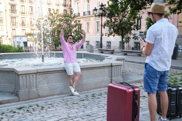Egy férfi, aki lefényképezi a boldog barátját a szökőkútnál egy városban.. — Stock Fotó