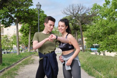 Parkta dikilirken akıllı bakışlara bakan neşeli genç spor çifti..