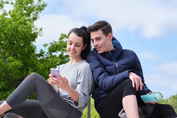 Boldog fiatal sport pár ellenőrzi az okostelefon, miközben ül a parkban — Stock Fotó