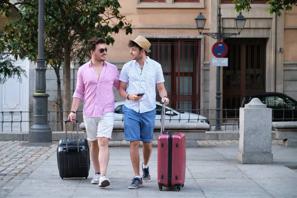 Homofile turistpar som frakter kofferter og drar til hotellet. – stockfoto