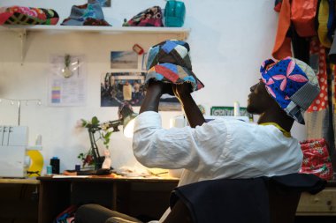 Siyah terzi dikiş dükkanında yaptığı şapkayı inceliyor. Afrika dikiş atölyesi.