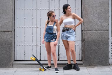 İki havalı kadın kaykayla bir tarafa bakıyor. Sokakta poz veren iki bayan arkadaş..