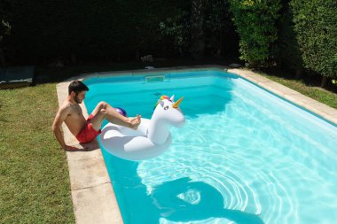 Genç adam şişme bir halkayla yüzme havuzuna giriyor. Yaz konsepti.