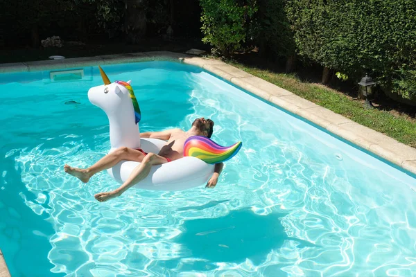 年轻男子在一个大独角兽充气环在游泳池 夏季概念 — 图库照片
