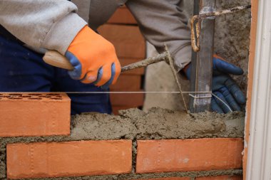 İnşaat işçisi tuğla duvara çimento koyuyor. Tuğla döşeme. Mason tuğla döşüyordu.