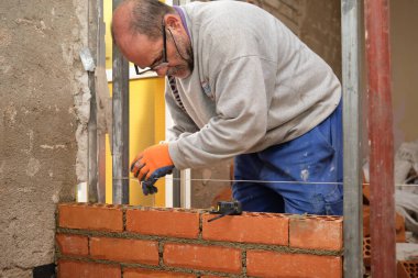 İnşaat işçisi düz bir duvar inşa etmek için ölçü alıyor. Tuğla döşeme. Mason tuğla döşüyordu.