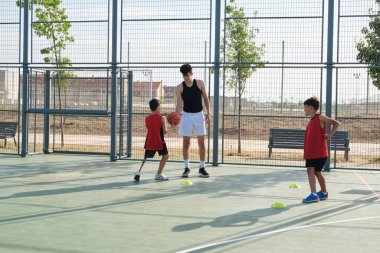 Older brother giving a basketball to his younger sibling with a leg prosthesis. Three brothers playing basketball.