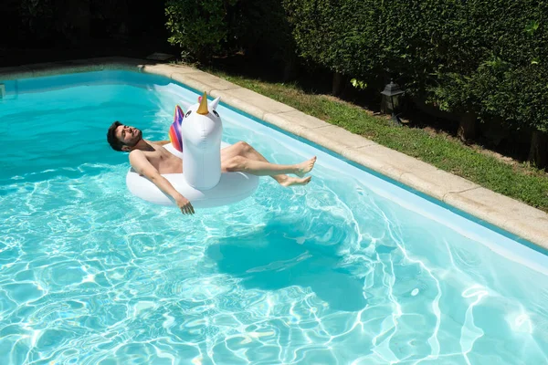 年轻人赤身裸体躺在游泳池里的大独角兽充气环上 夏季概念 — 图库照片