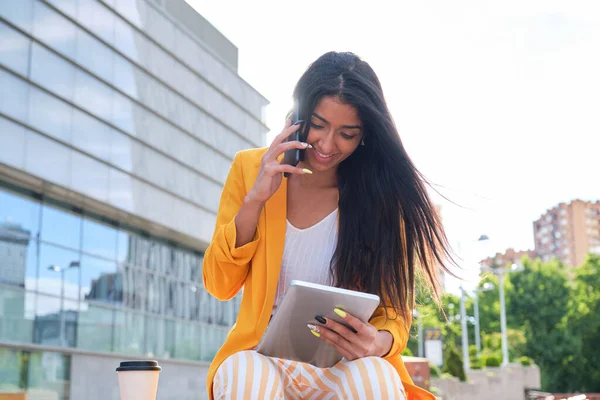 Молода латинська бізнес-леді працює з планшетом і розмовляє по телефону на відкритому повітрі . — стокове фото