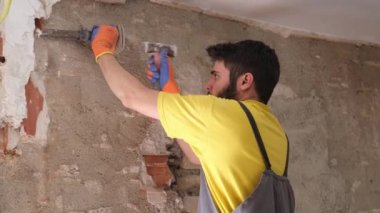 Genç inşaatçı çekiç ve keskiyle bir ev duvarını yıkıyor..